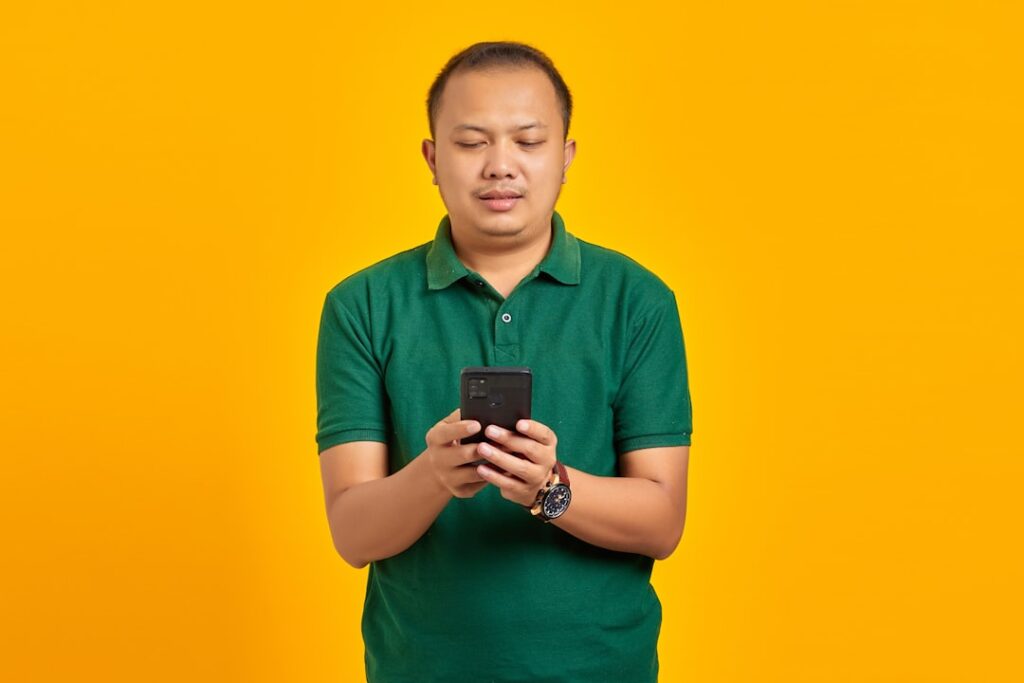 Um Homem Em Uma Camisa Verde Olhando Para Um Telefone Celular BSDhhz K6OU