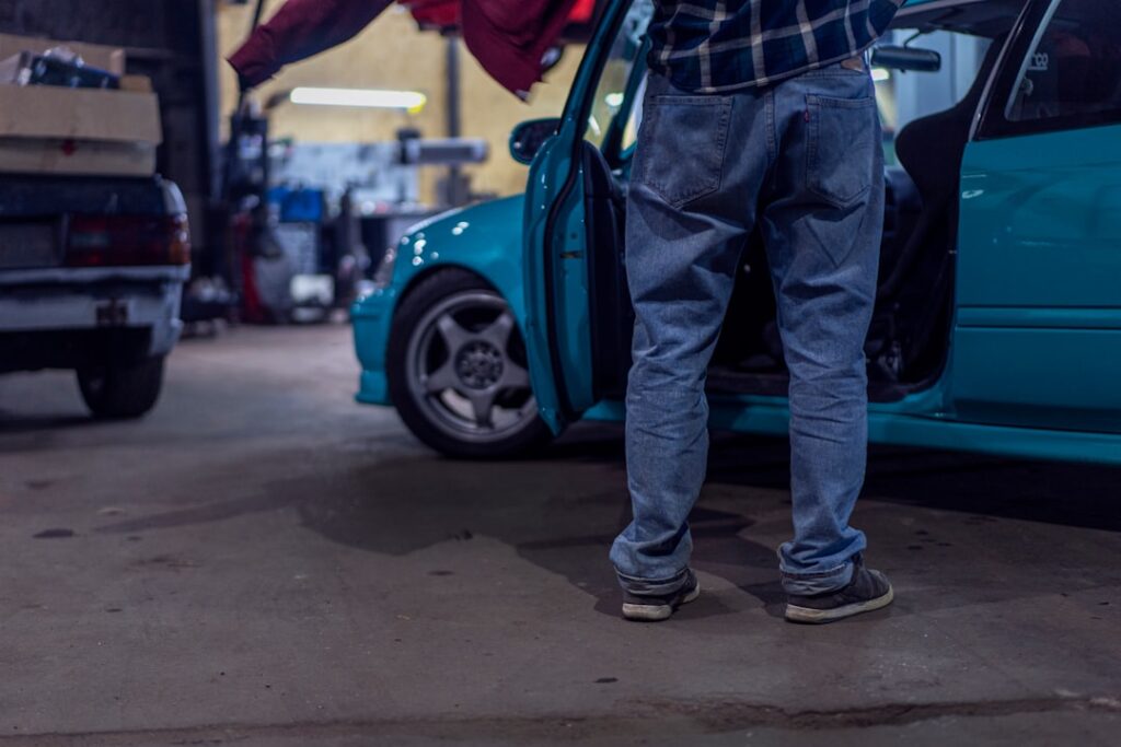 Homem Em Jeans Azuis E Botas De Couro Preto De Pe Ao Lado Do Carro Azul Durante O Dia XwQyWSSISeg